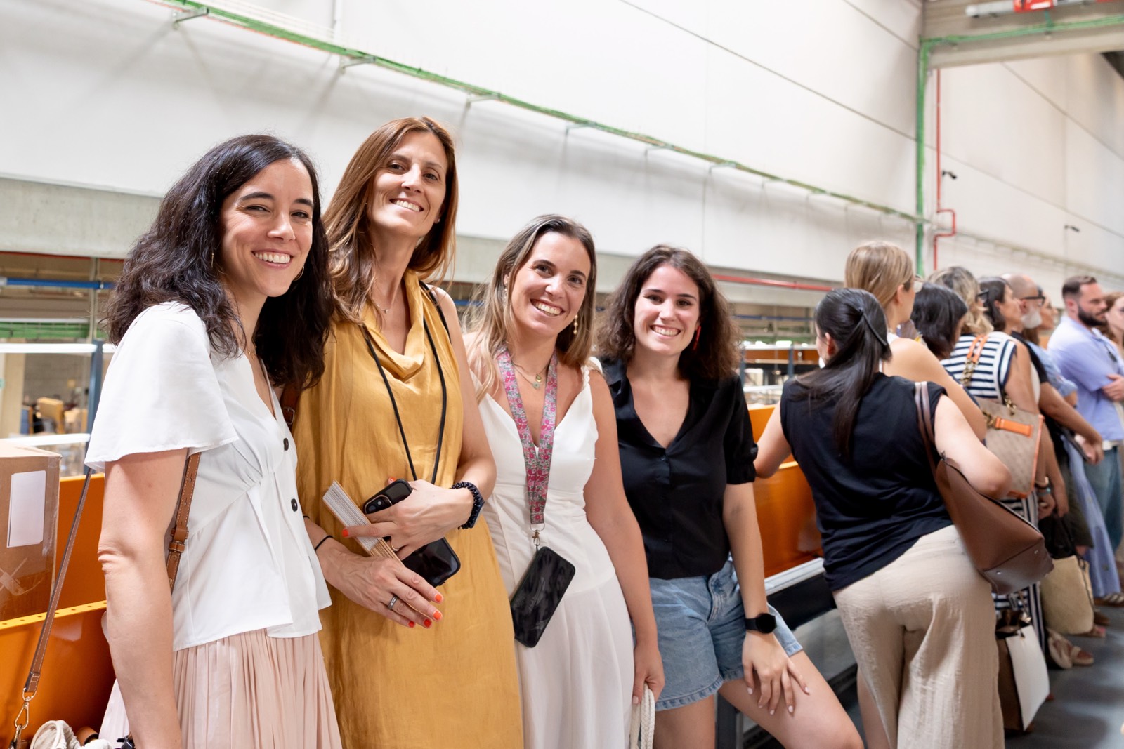 Cuatro mujeres sonrientes posando juntas en un evento, con otras personas de fondo en un espacio interior