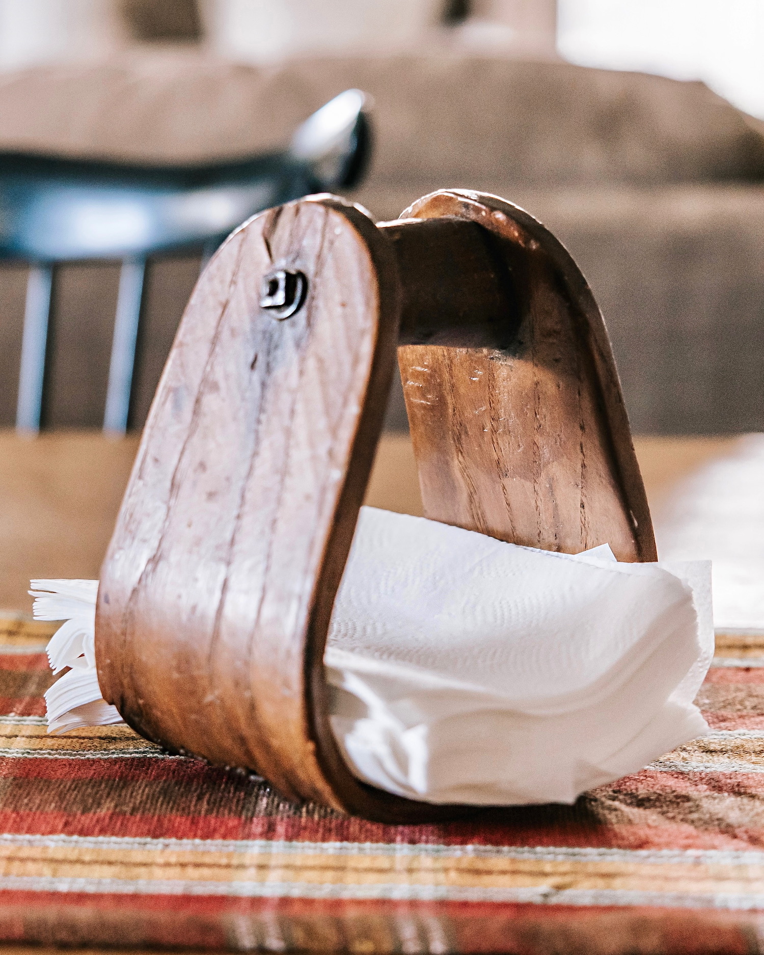 Servilletero de madera vintage con servilletas blancas sobre una mesa con mantel a cuadros rojos. El servilletero tiene un acabado rústico y forma curva tradicional.