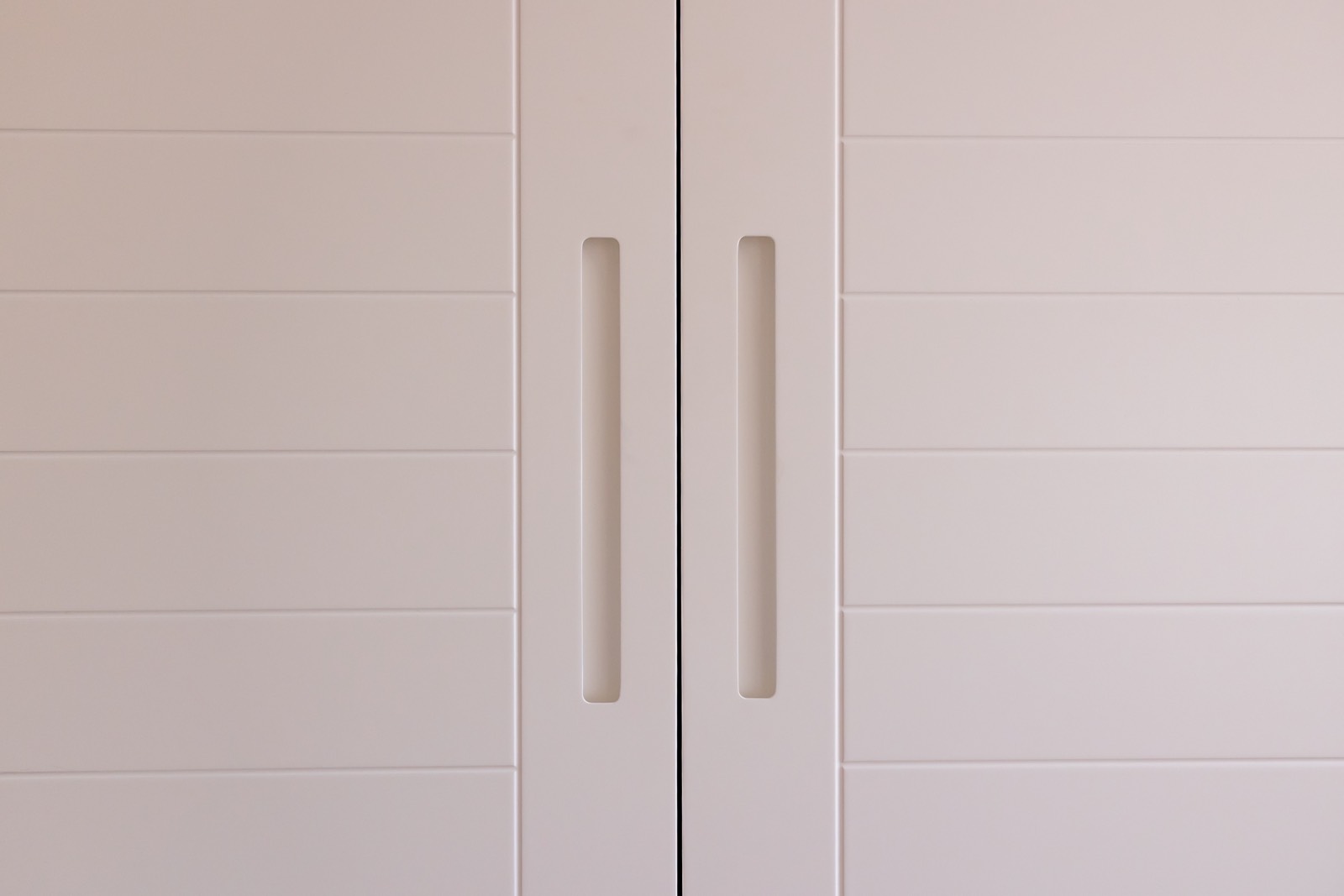 Primer plano de dos puertas de armario blancas con manijas verticales empotradas y diseño minimalista