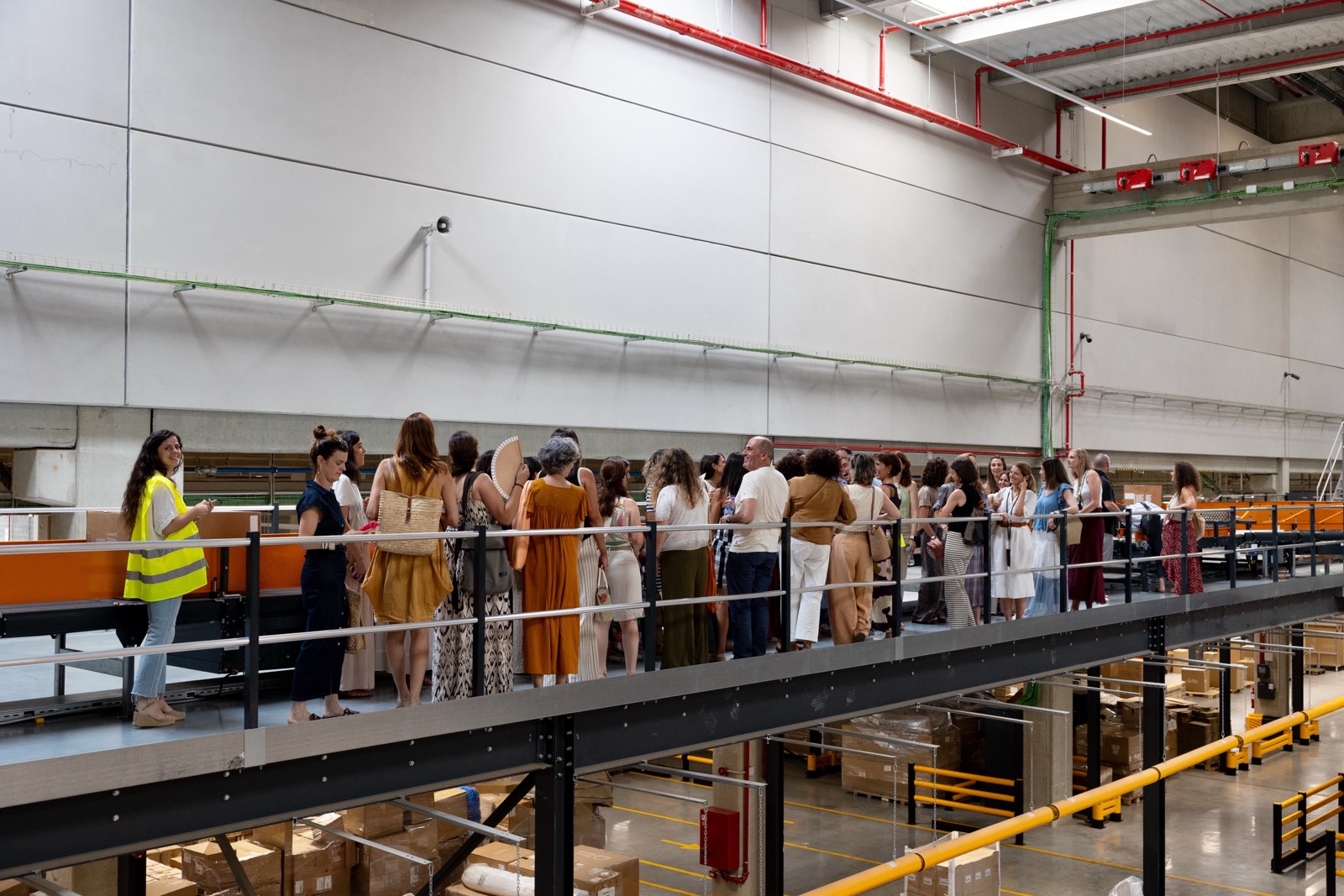 Grupo de personas en un pasarela elevada observando un almacén logístico con cajas y estanterías
