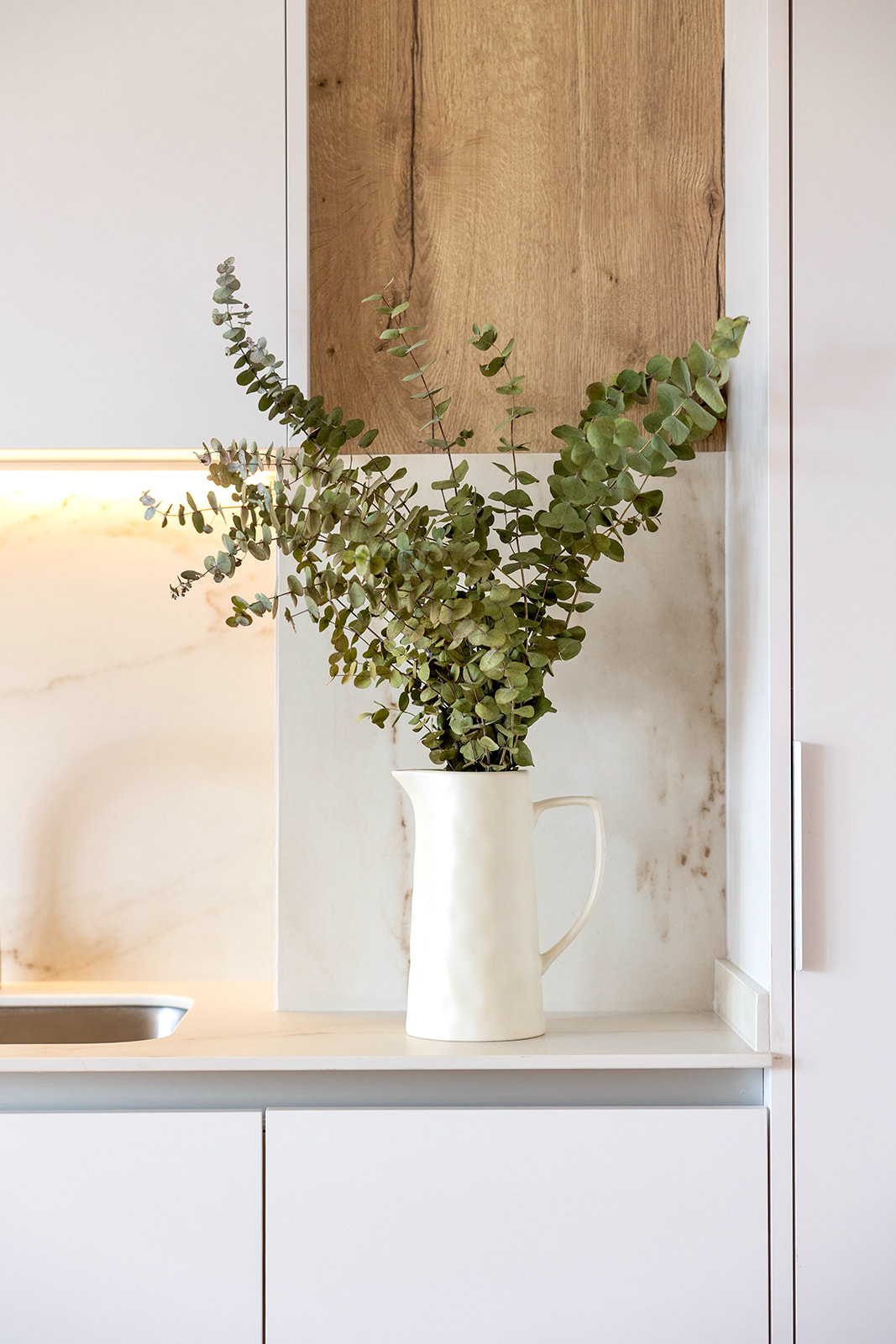 Ramas de eucalipto en una jarra blanca sobre una encimera de cocina moderna con detalles en madera