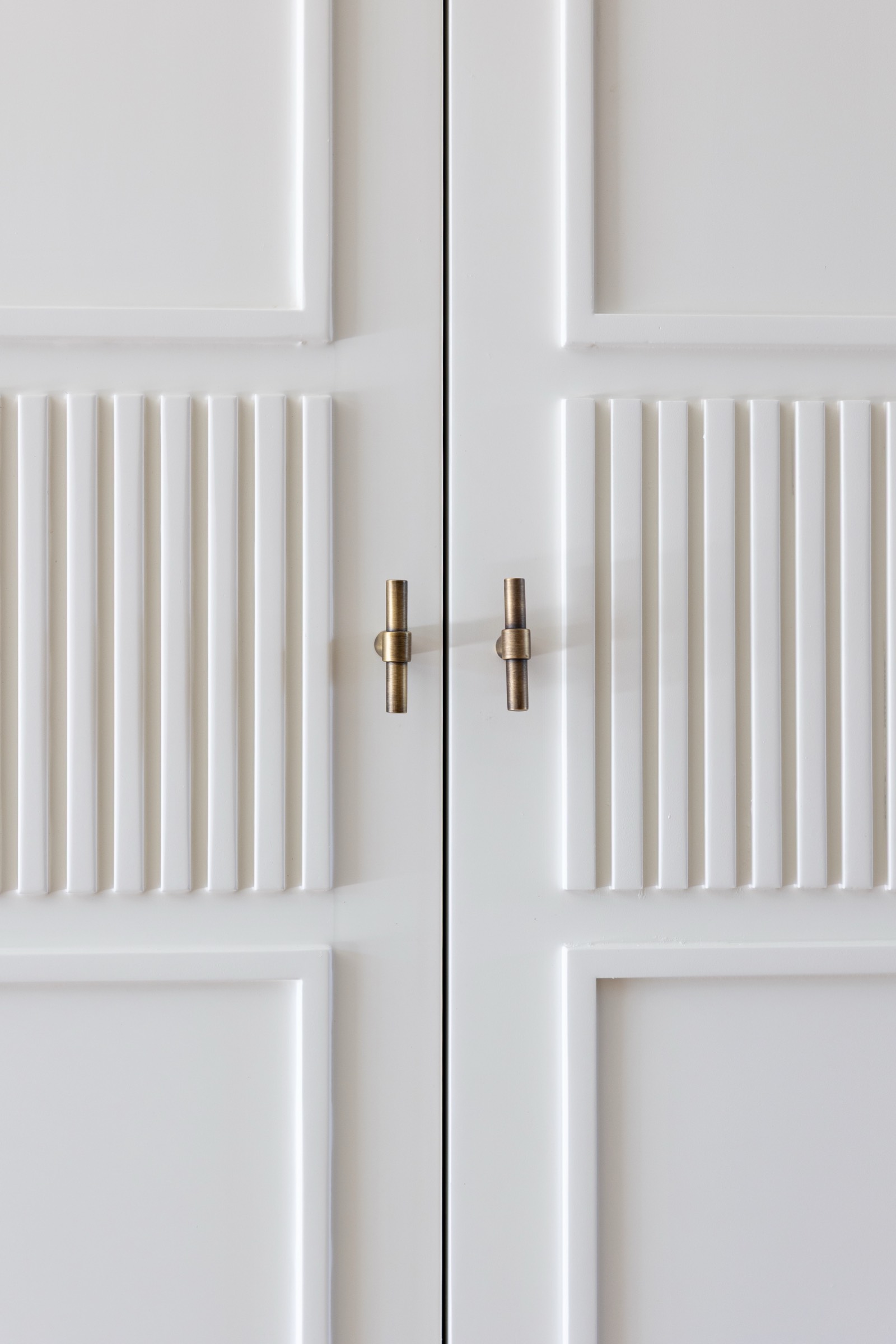 Primer plano de dos puertas blancas con paneles verticales y horizontales, con elegantes manijas doradas cilíndricas