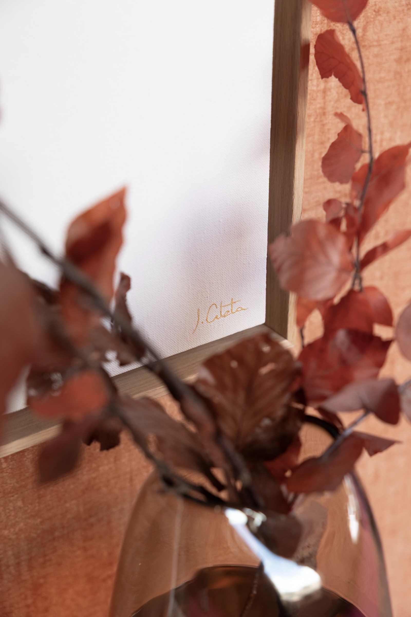 Ramas de hojas rojas otoñales en un florero de vidrio con un marco en el fondo, capturadas en tonos cálidos y suaves