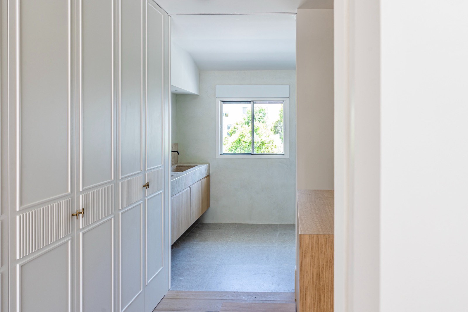 Espacio interior de cocina minimalista con armarios blancos, encimera y ventana con vista a vegetación verde