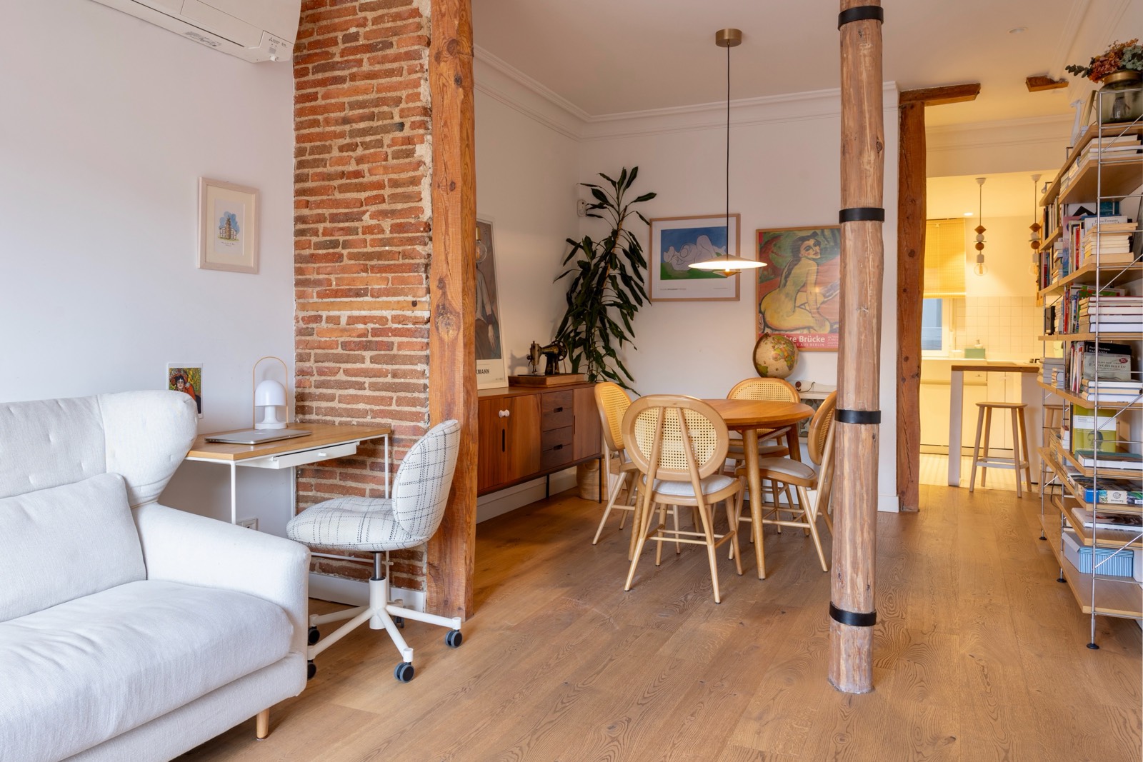 Espacio interior de apartamento luminoso con elementos de diseño de madera, ladrillo expuesto, sofá blanco, mesa de comedor y estantería