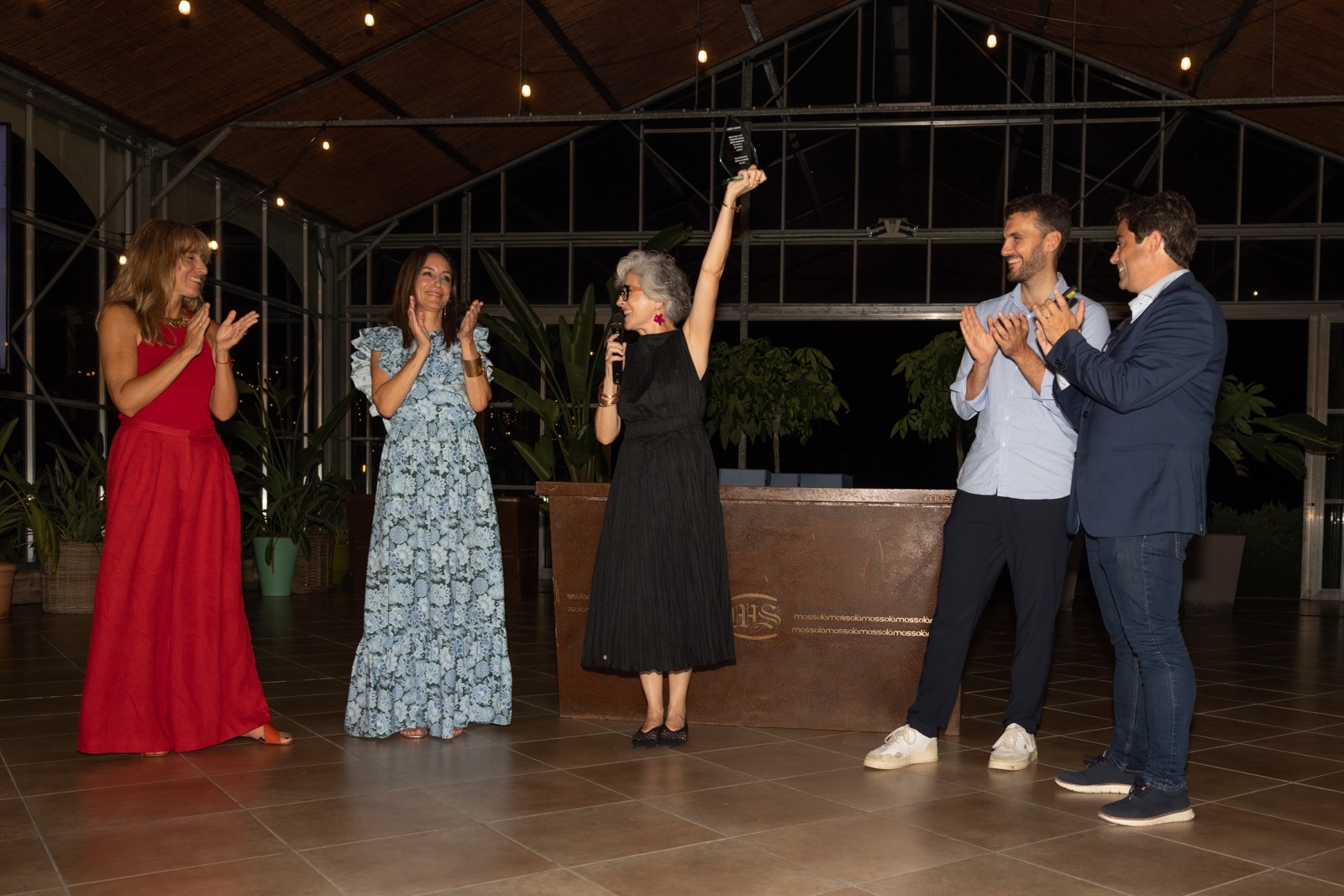 Grupo de personas elegantemente vestidas en un evento, con una persona sosteniendo un premio y todos aplaudiendo