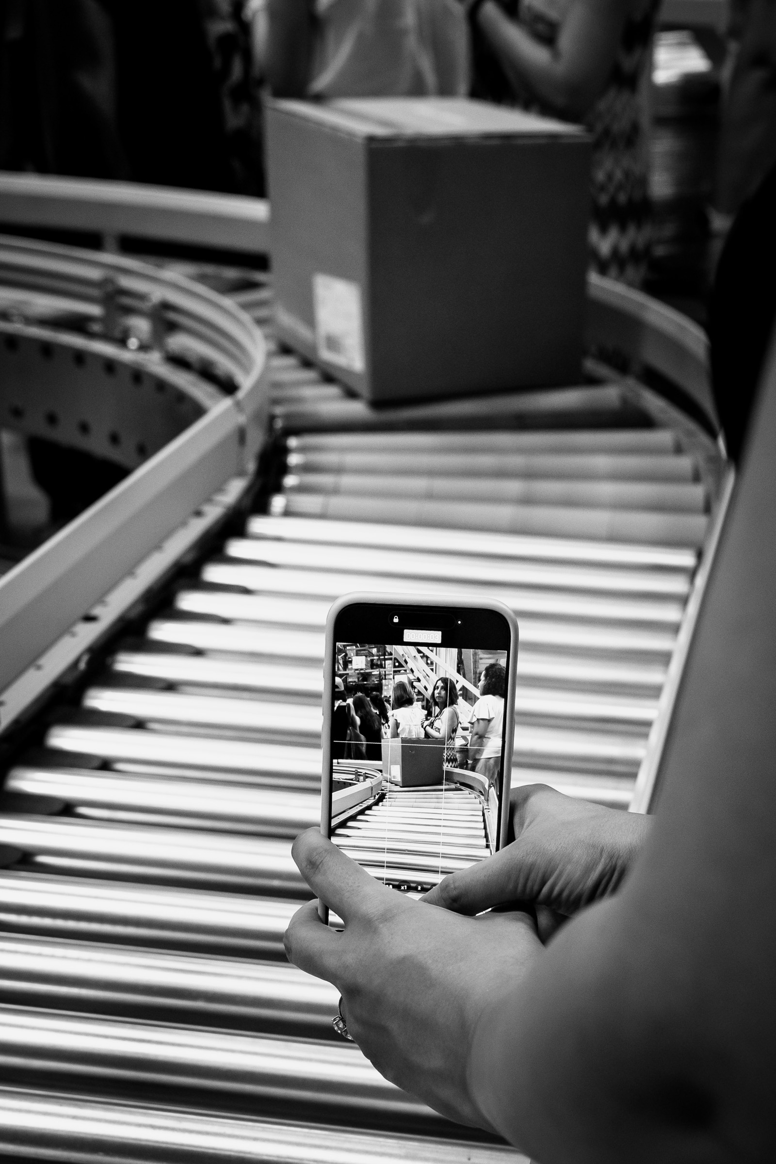 Mano sosteniendo un teléfono móvil que captura una imagen de una banda transportadora en blanco y negro