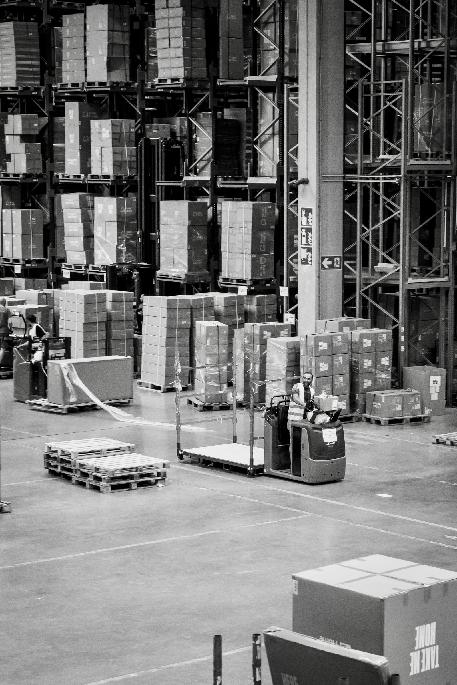 Vista interior de un almacén industrial con estanterías altas, cajas apiladas y un operario conduciendo un montacargas