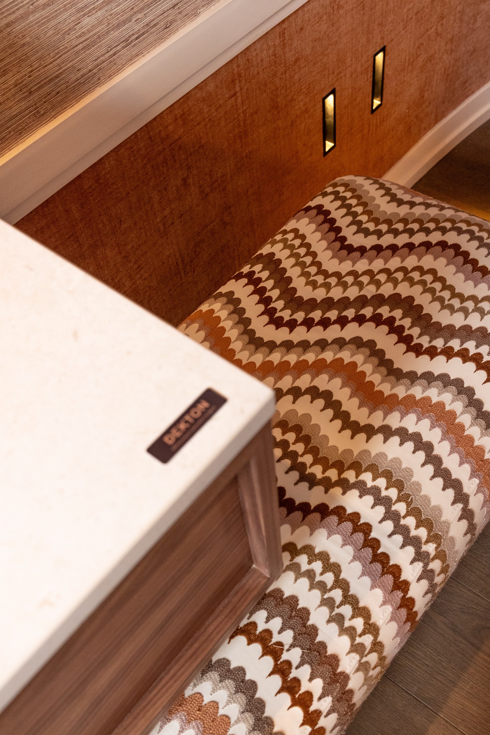 Detalle de diseño interior con superficie de madera marrón y tapizado con patrón ondulado en tonos marrones y blancos