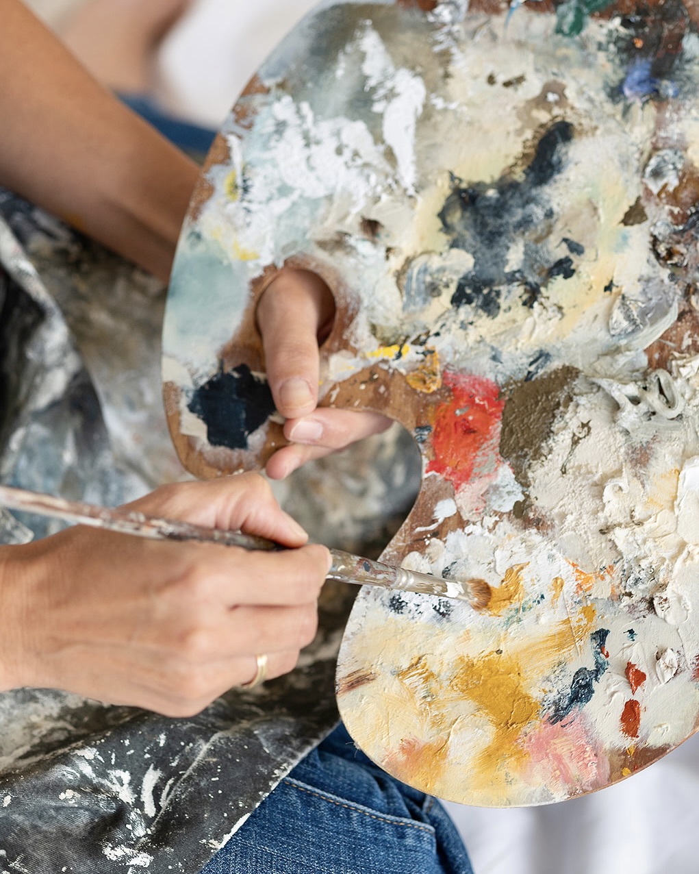 Primer plano de manos sosteniendo una paleta de pintor con varios colores mezclados. Un pincel se utiliza para mezclar las pinturas en la paleta, mostrando el proceso creativo del artista.
