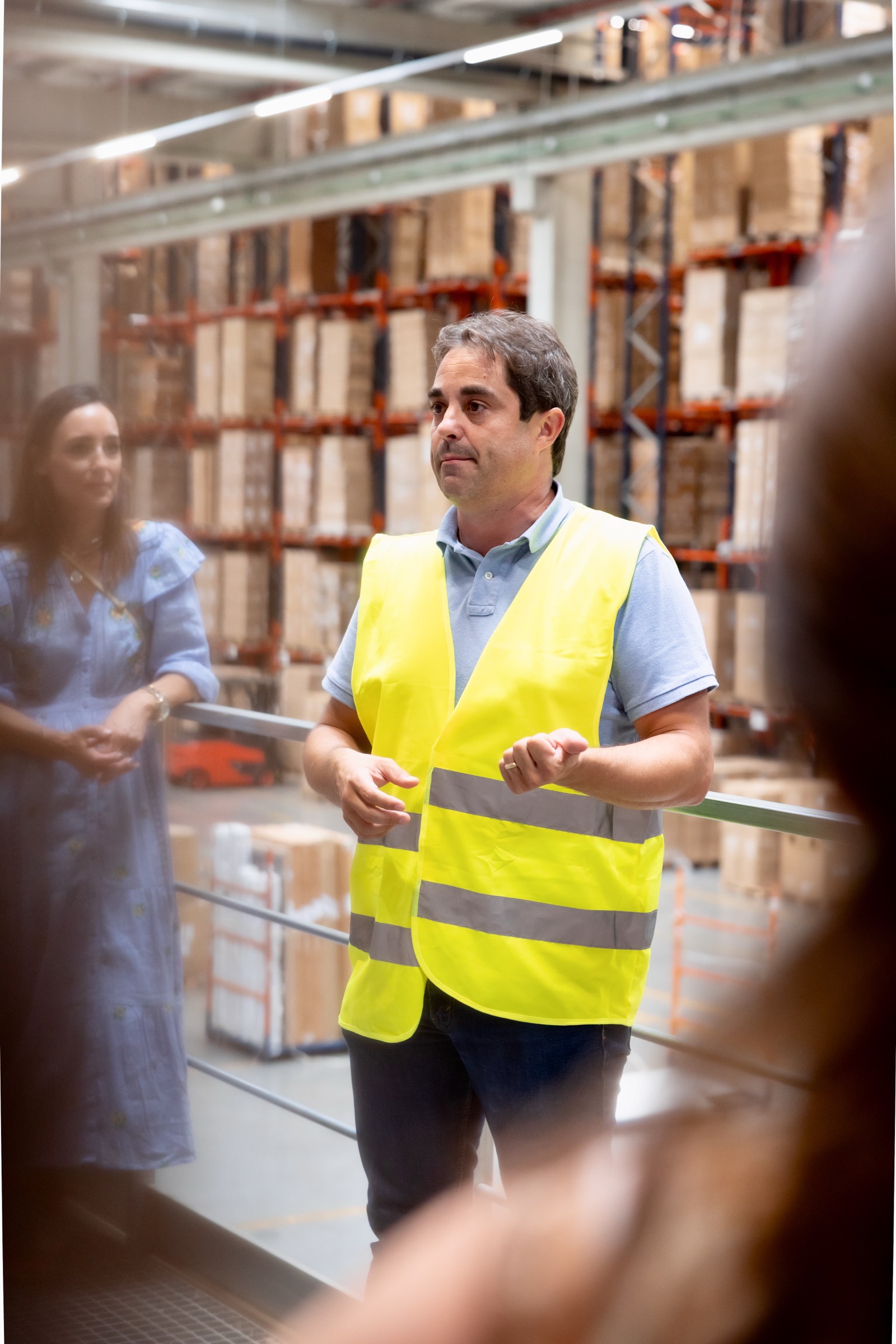 Trabajador con chaleco de seguridad amarillo en un almacén moderno, con estanterías de metal y cajas de fondo