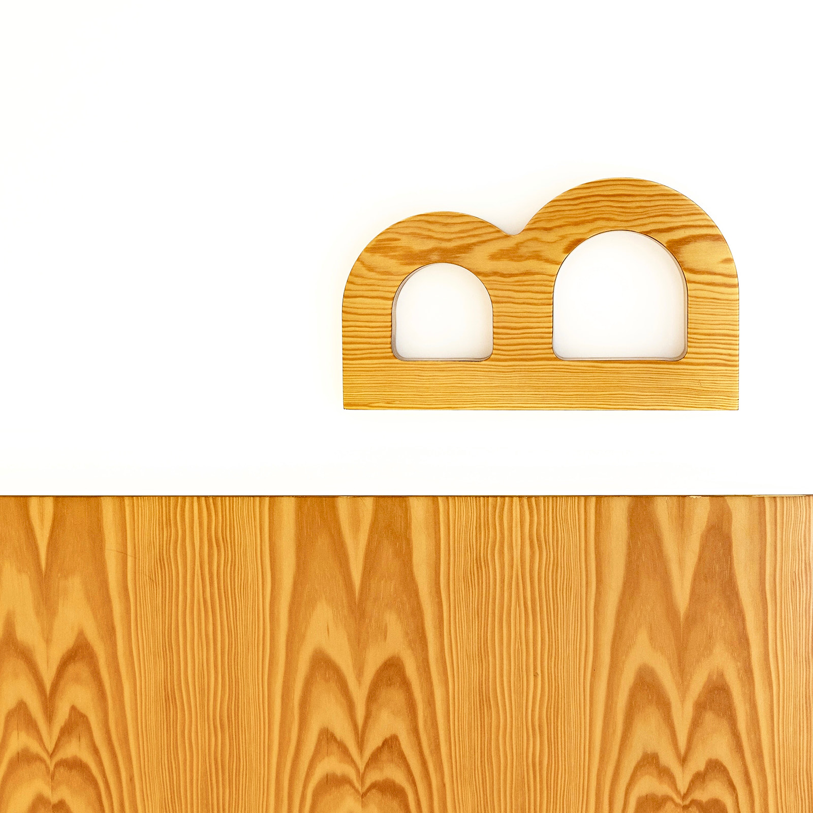 Letra B mayúscula hecha de madera clara con vetas visibles, colocada sobre un fondo blanco. Debajo hay una sección de madera con patrones de vetas más pronunciados.