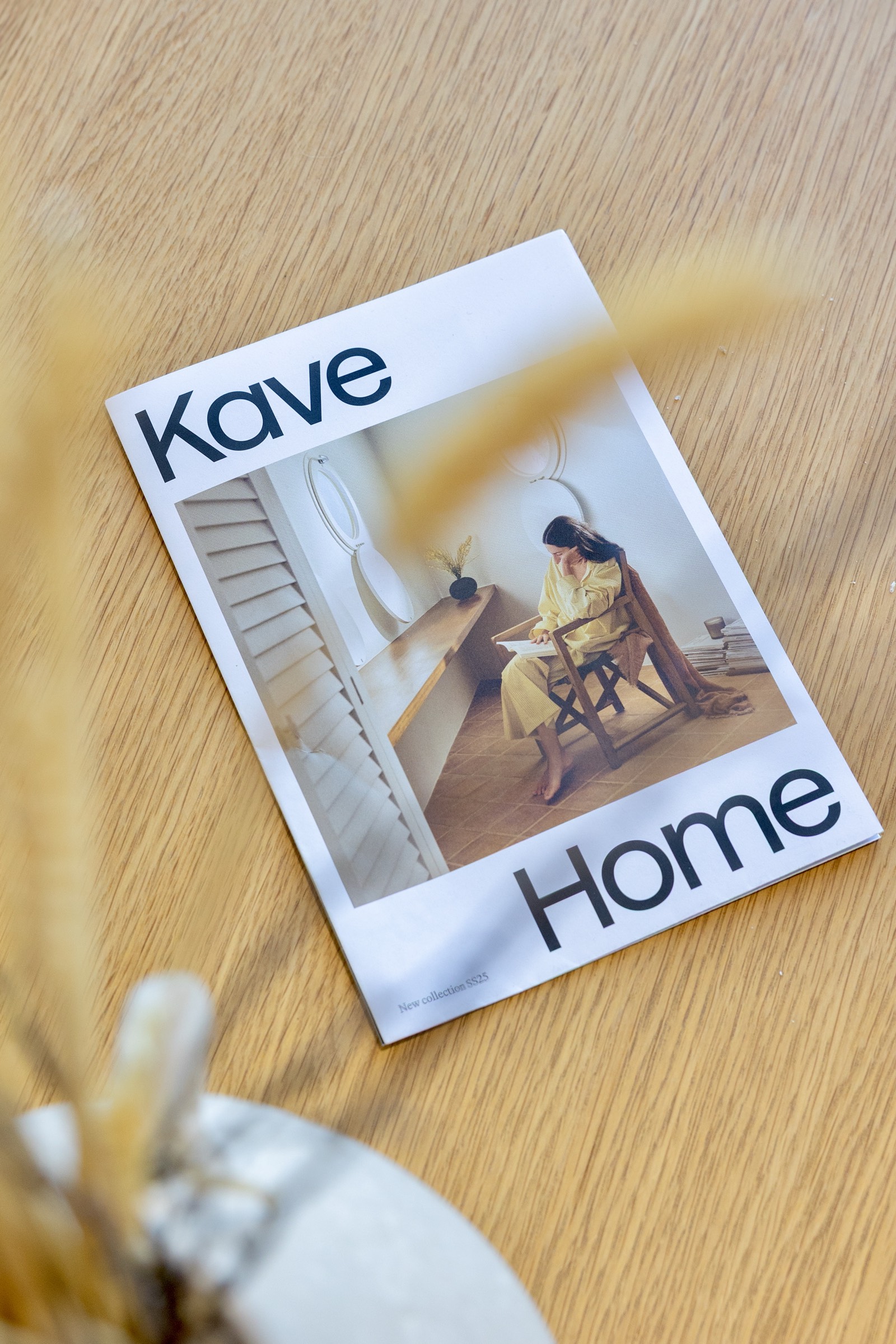 Portada de revista Kave Home con una imagen de una persona sentada en una silla de madera cerca de una escalera, sobre una superficie de madera