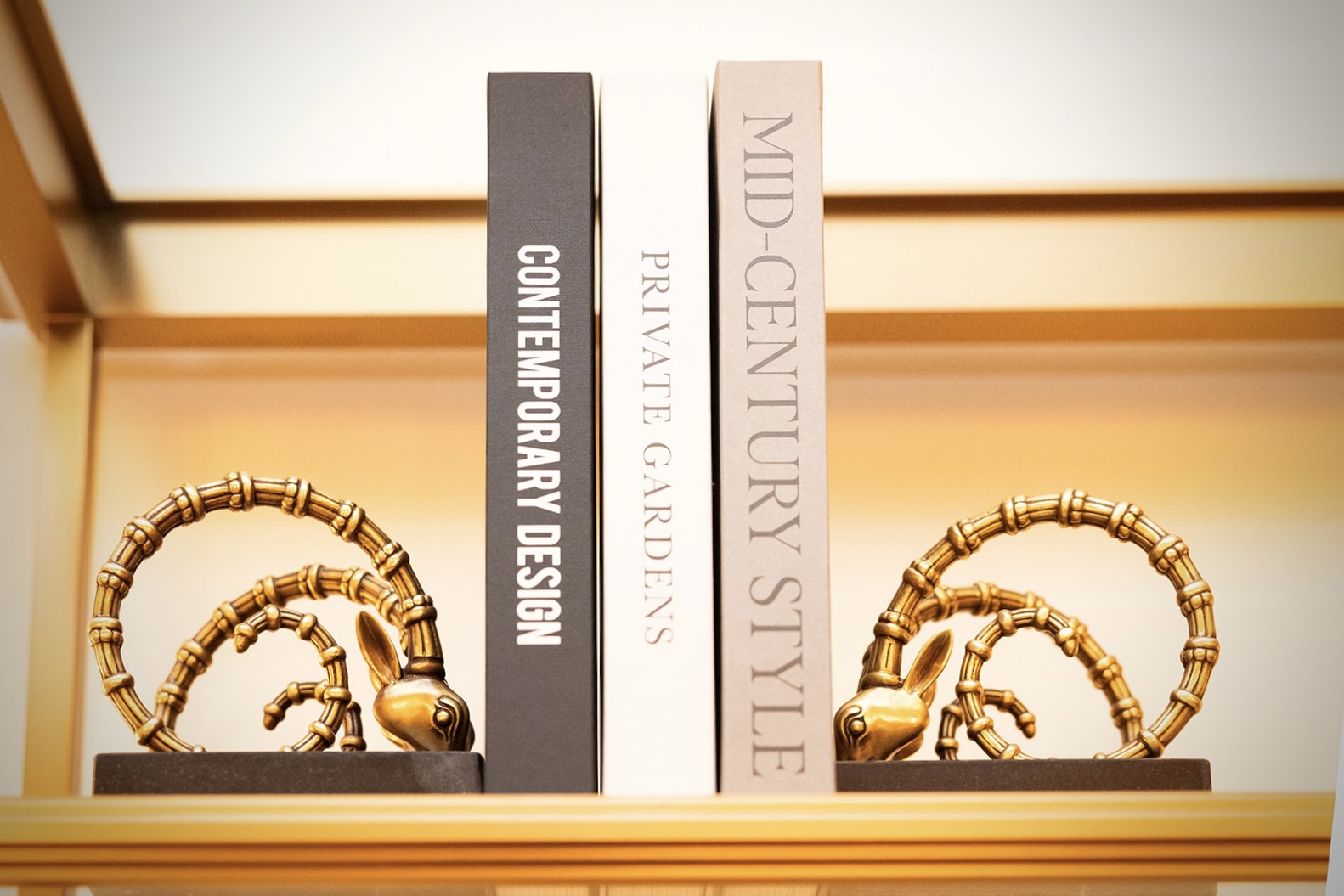 Estantería con tres libros de diseño y decoración sostenidos por sujetalibros en forma de cobras doradas estilizadas.