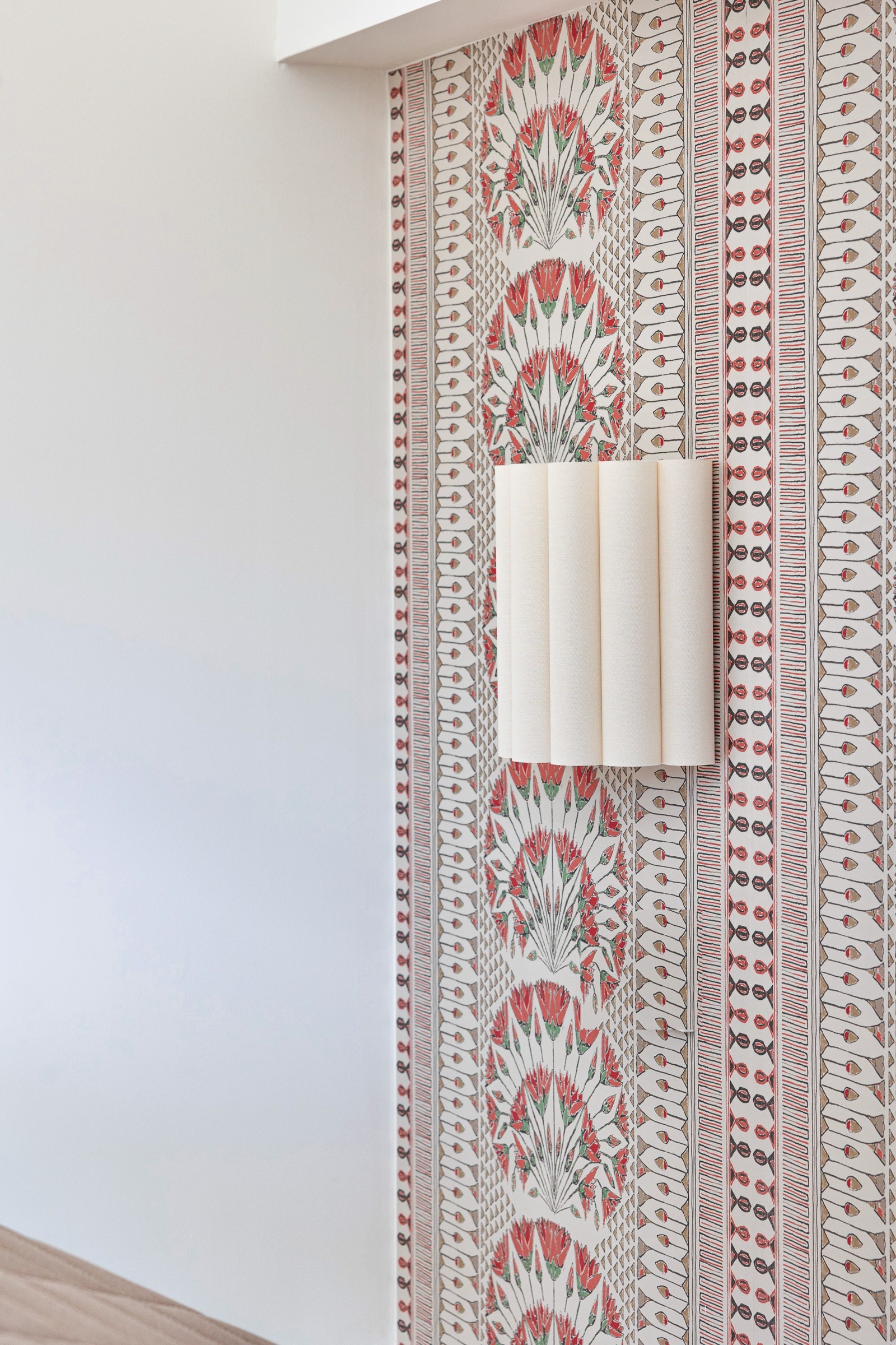 Pared con papel tapiz vintage de estilo ornamental con diseño de abanicos en tonos rojos, blancos y marrones, con una lámpara blanca moderna