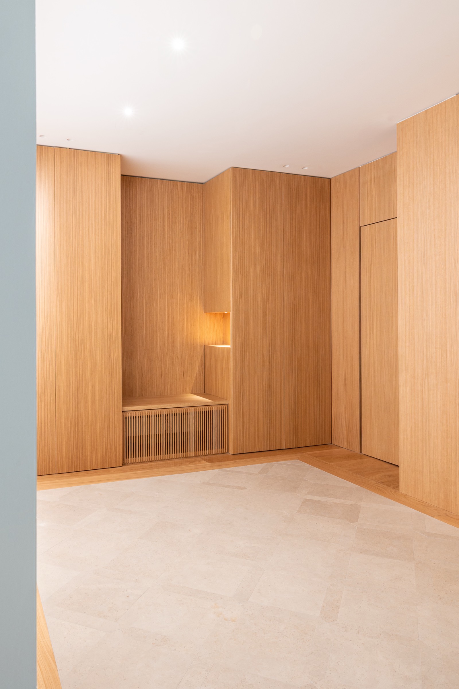 Espacio interior moderno con paredes de madera en tonos cálidos, piso neutro y una lámpara empotrada suave