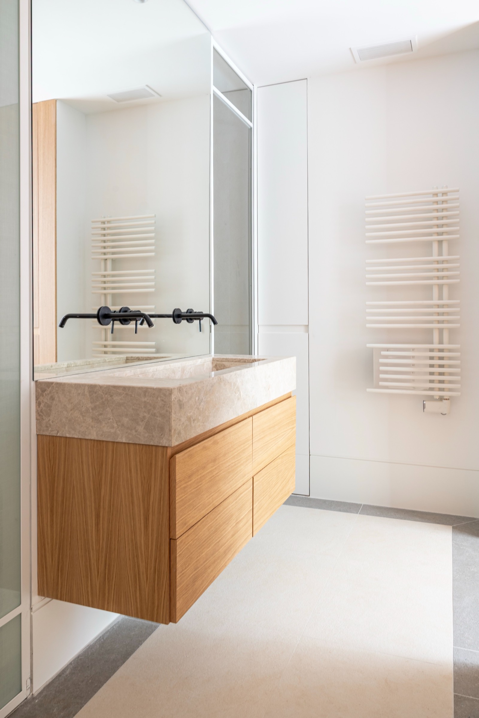 Baño minimalista con mueble de lavabo de madera, encimera de piedra beige, espejo y toallero blanco moderno