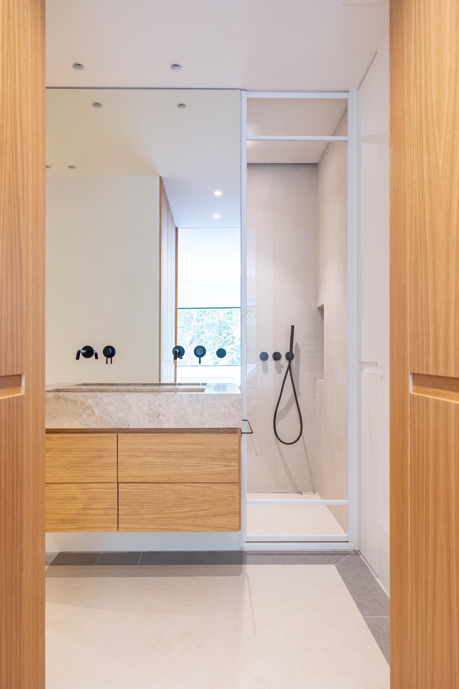 Interior de cuarto de baño minimalista con ducha de vidrio, mueble de madera y paredes blancas con detalles en negro