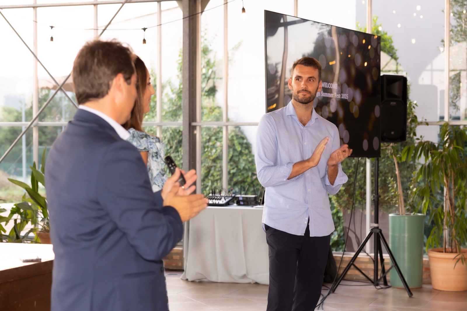 Dos profesionales en una reunión dentro de un espacio acristalado con plantas, uno de pie haciendo un gesto mientras conversa con otro