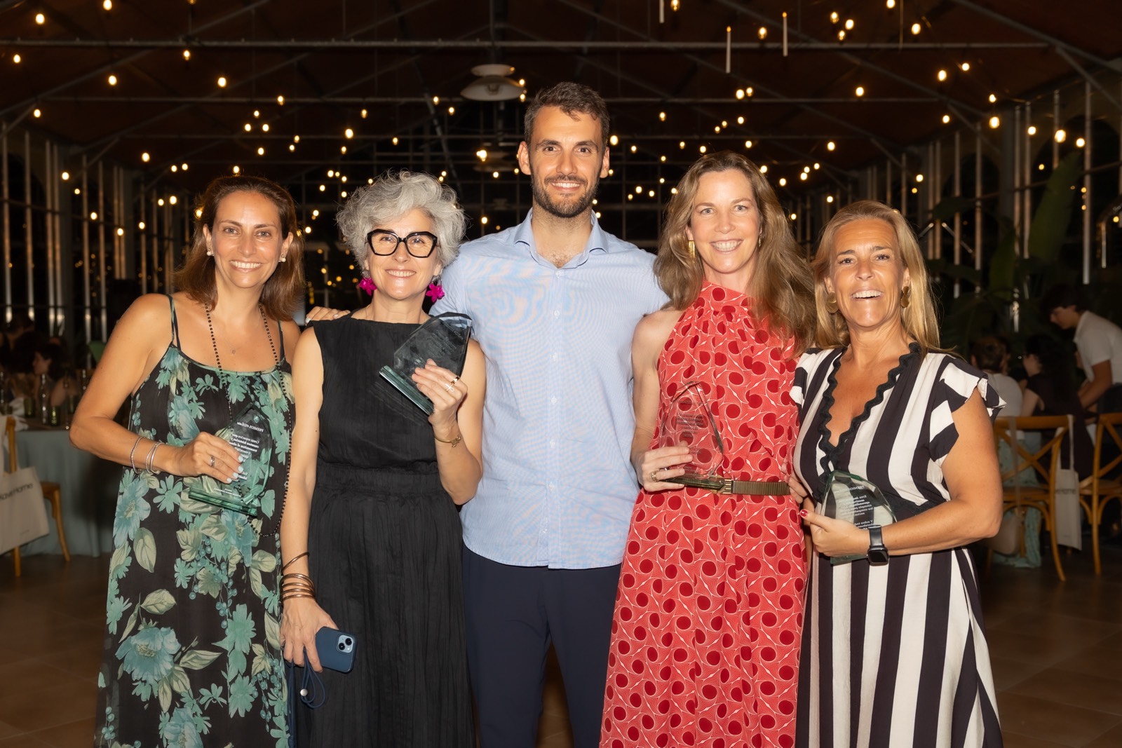 Cinco personas sonrientes posando juntas en un evento con iluminación cálida de luces colgantes