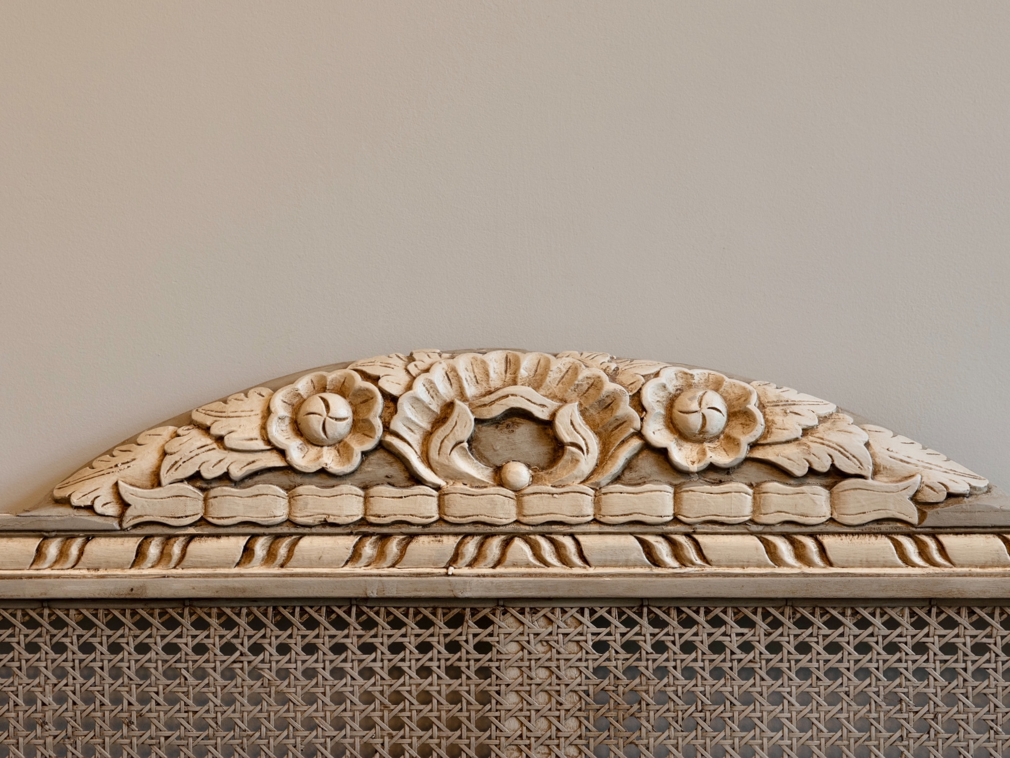 Detalle arquitectónico de talla en madera con diseño floral en estilo vintage, mostrando flores decorativas y motivos ornamentales sobre un respaldo de rejilla